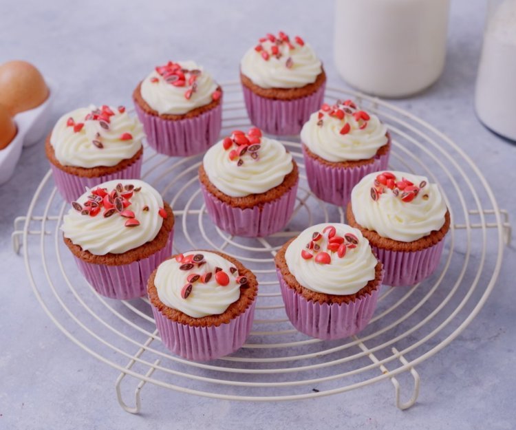 Cupcakes staan op een witte taartrooster om af te koelen. Ze zijn afgewerkt met mooie toefjes frosting en gecrushte rode smarties.  