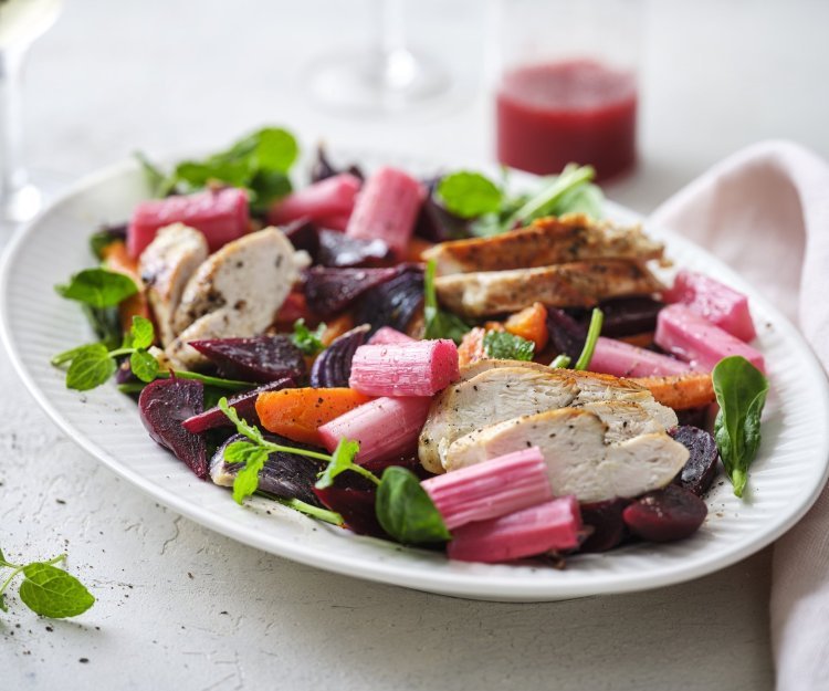 Salade met rabarber, kip en frambozendressing Een rijkgevuld salade die gezond is en mooi van kleur, daar word je instant vrolijk van. De salade bestaat uit frisgroene spinazie, warmoranje wortel, bloedrode bietjes, zoetroze rabarbar en goudgegrilde kip. De frambozendressing werd erbij geserveerd in een glazen kannetje.