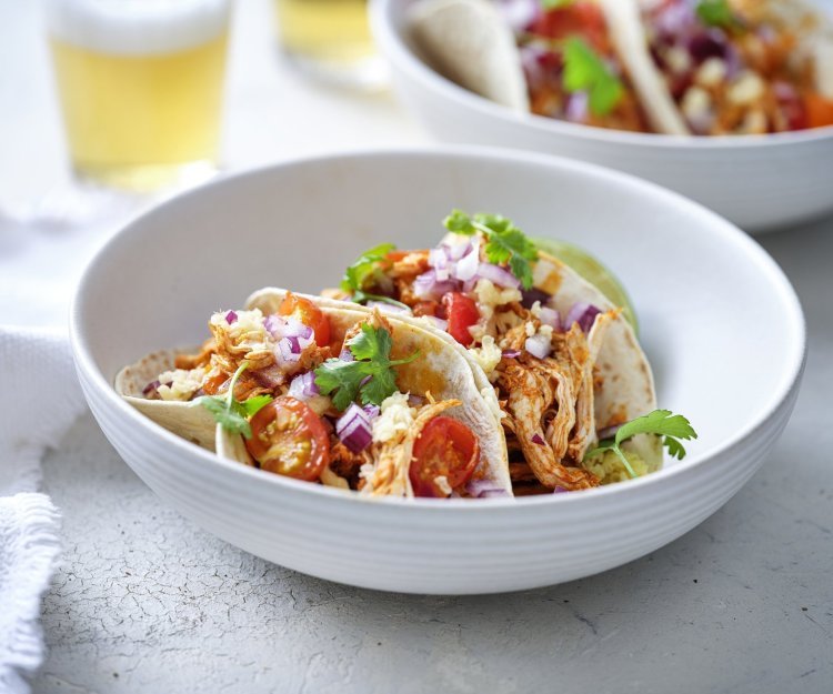 Taco’s met pulled chicken, tomaatjes, rode ui en Passendale kaas In een diep wit bord liggen twee gevulde taco's met pulled chicken, afgewerkt met tomaat, rode ui en geraspte Passendael kaas. Om wat extra kleur te geven liggen er enkele blaadjes koriander op. Wij serveren ze met frisgekoeld biertje, smakelijk!