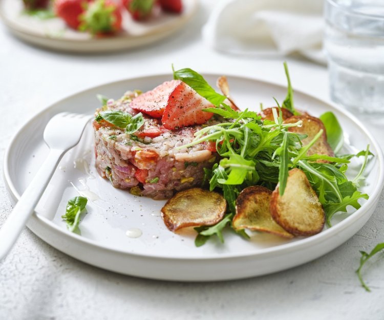 Tartaar van kalfsvlees met aardbei en aardappelplakjes Zoek je een alternatief voor steak-tartaar? Wel dit is een zomerversie, nl eentje met kalfsvlees, aardbeien, tomaatjes en verse kruiden. We werkten het gerechtje af met gebakken aardappelplakjes en verse rucola. Er ligt een wit vork en servette naast om meteen aan te vallen.