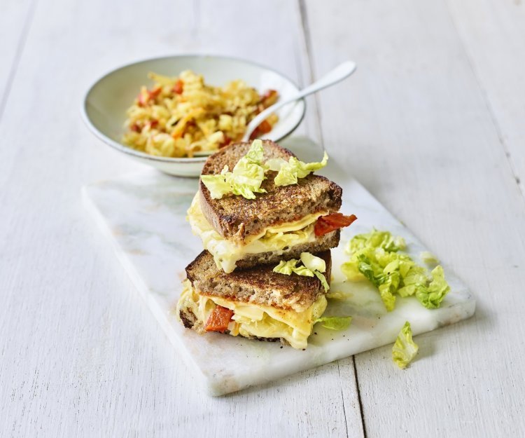 Toast met kazen van bij ons, kimchi en chilisaus Een heerlijke cheesy toast ligt op een marmere snijplank. De toast is gevuld met 2 Belgische kazen, kimchi en chilisaus.