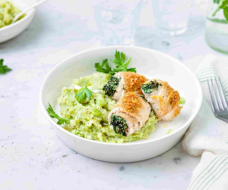 Gevulde tongrolletjes met spinazie en ricotta liggen op een groene puree van broccoli en aardappel. Ze liggen in een diep bord waarbij een karaf- en waterglas langs staat.