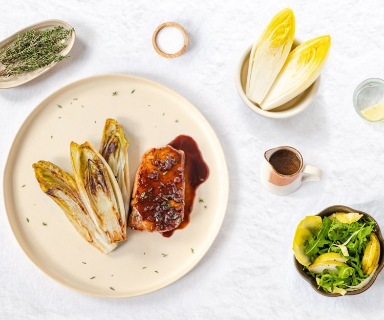 Varkensmignonette met witloof en Luikse saus Gestoofd witloof ligt naast een heerlijk stukje varkensvlees gepresenteerd. De luikse saus kleurt heerlijk zoetbruin.