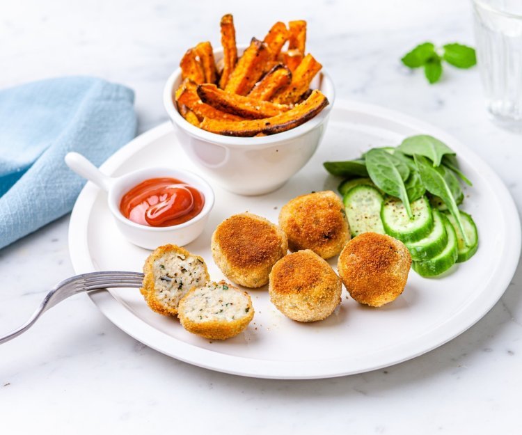 Visballetjes van wijting met pompoenfrietjes Visballetjes van wijting liggen op een wit bord met frietjes van pompoen erbij. Er staat ook een potje ketchup langs en een lichtblauwe servette.