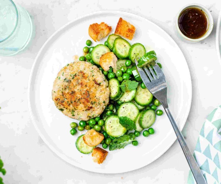 Visburger van heek met komkommer en erwtjessalade Een burger van vis? Yep, dit is er eentje van heek met een groene salade van erwtjes en komkommer. Langs het bord staat een klein sauspotje met de vinaigrette om zelf toe te voegen.