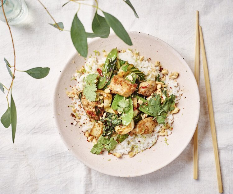 Een portie food is uitgeschept in een licht roze bord. Het is een portie rijst met daar bovenop de wok van konijn met paksoi en peultjes. Om af te werken zijn er wat pindanootjes toegevoegd en koriander.