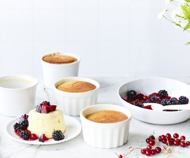 Er staan 4 soufflés op tafel, waarvan al eentje uit zijn ovenpotje. Het rood fruit ligt er langs, denk maar aan aardbeien, bessen en pruimen.