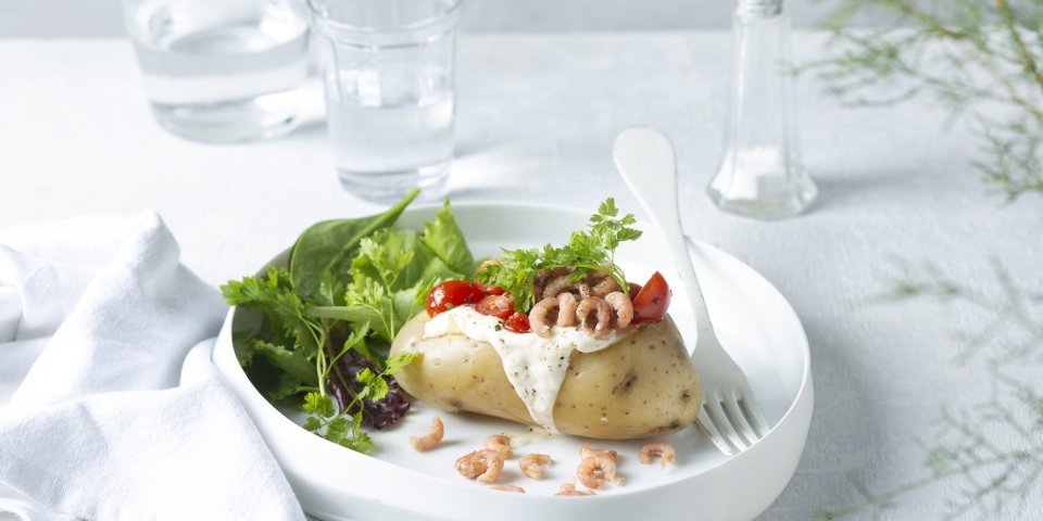 Aardappel in de schil met zure room, garnalen en kerstomaatjes Een gepofte aardappel feestelijk afgewerkt met zure room, garnaaltjes en kerstomaatjes. Het gerechtje is afgewerkt met een groene salade dat instant kleur geeft aan het gerecht.