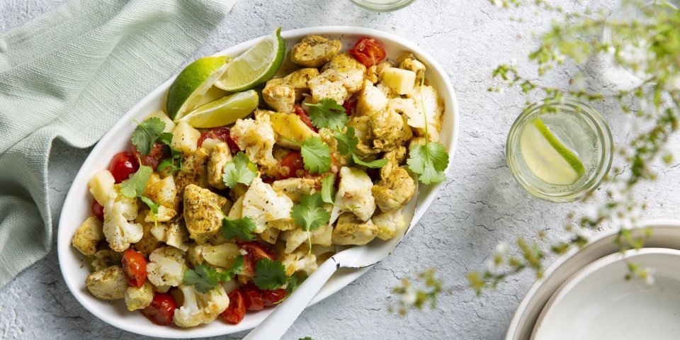 Aloo gobi is een Indiase curry van aardappel en bloemkool. Wij deden er nog stukjes kip bij. Deze rijkgevulde schotel van groenten en kruiden staat op tafel met een grote witte lepel bij. Voor de afwerking werd deze schotel gepresenteerd met korianderblaadjes en limoenpartjes. 