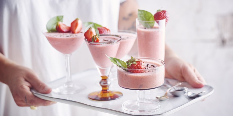 Bavarois van aardbei met basilicum en zwarte peper Roze bavarois geserveerd in verschillende glaasjes op een dienplateau. Een vrouw met witte t-shirt draagt deze roze dessertjes, klaar om naar de gasten te brengen.