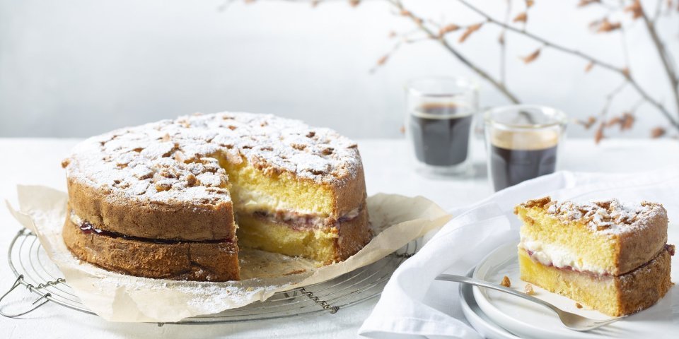 Biscuit met vanillepudding en slagroom Een biscuit met vanillepudding en slagroom staat op tafel op een taartrooster. Er is al een stukje aangesneden om de lijnen duidelijk te laten zien van de pudding en slagroom. Koffie uitgeschonken, vorkje prikken en aanvallen die taart.