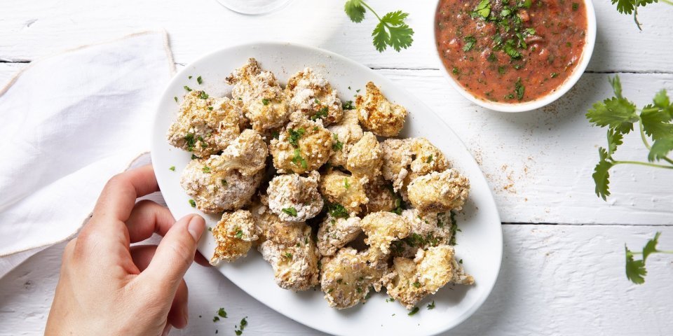 Krokante bloemkoolroosjes als aperitiefhapje, liggen klaar op een ovaal wit bordje. Er staat een pittige tomatensaus langs om te dippen. Tijd voor de apero te starten. 