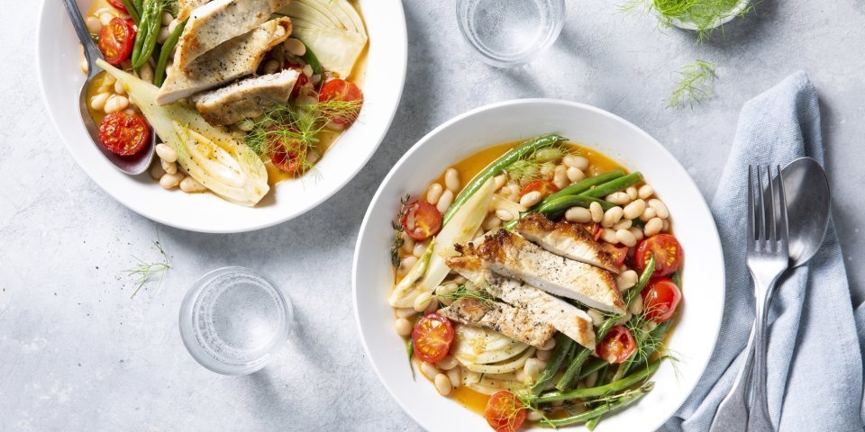Bouillon van tomaat en venkel met boontjes en varkenskotelet Bouillon met stukjes groenten en varkensvlees. De tomaten en boontjes zorgen voor een mooi kleurrijk bordje. De soep is uitgeschonken in twee diepe witte borden.