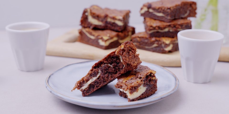 De browniecheesecake ligt op een bordje aangesneden. Dit is eigenlijk een brownie in combinatie met cheesecake, zo verkrijg je een marmereffect in je brownie door het mengsel met de roomkaas. 
