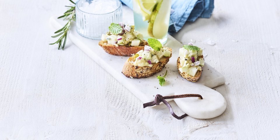 Bruschetta met perensalsa en blauwe schimmelkaas liggen op een marmer schaaltje samen met een homemade rozemarijnlimonade met peer. 