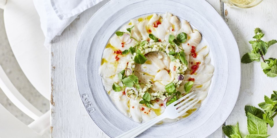 Ceviche van wijting, koolrabi en appel Ceviche van wijting met kleine stukjes koolrabi en appel er bovenop. Hij is geserveerd op een wit bord waardoor de groentjes nog extra opvallen. Er ligt verse munt langs en een witte servette.