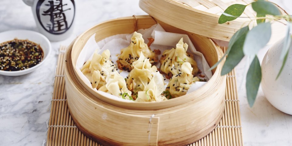 Er staat een stoommandje op het marmere aanrecht waarin verschillende dumplings liggen. Er staat bovenaan een dipsausje op basis van sojasaus en een chinees kannetje. 