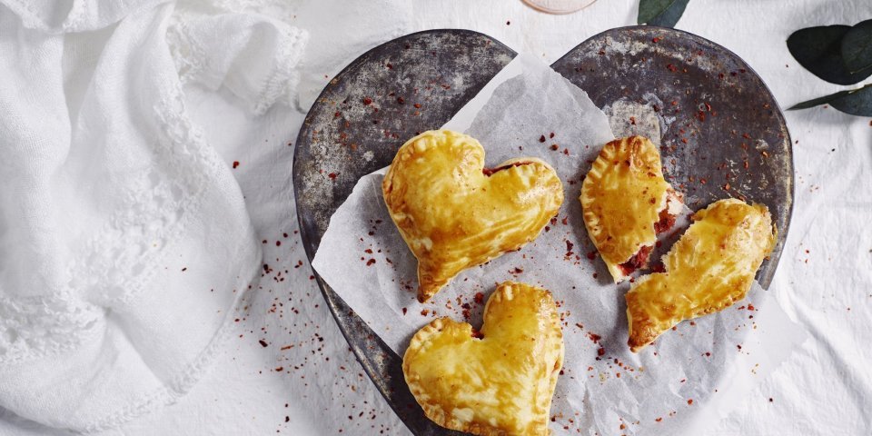 Empanadas gemaakt in hartjesvorm liggen op een bordje te schitteren. Met dit hapje scoor je sowieso bij je geliefde. 