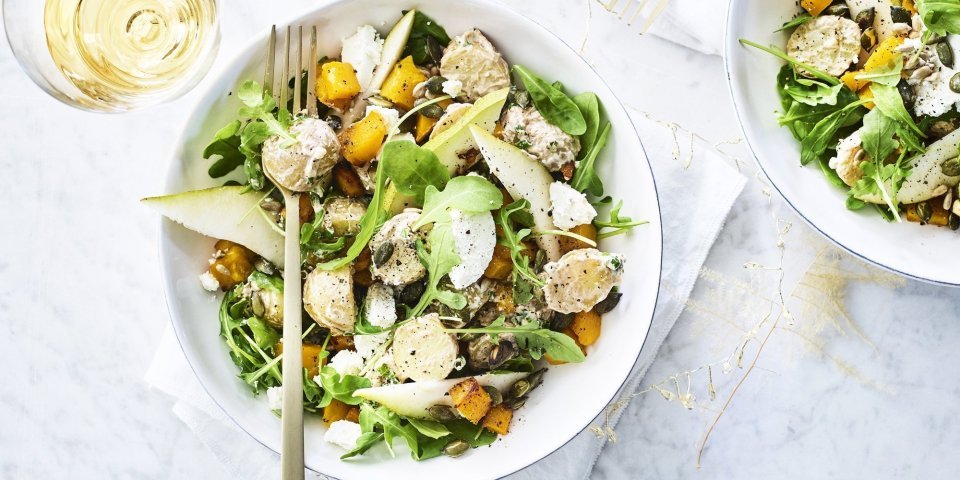 Een heerlijke aardappelsalade geserveerd in een diep wit bord. De kleuren zijn heerlijk fris en zonnig om je feestmenu te laten stralen. Groen, oranje en wit zijn hier de kleurtoppers. 