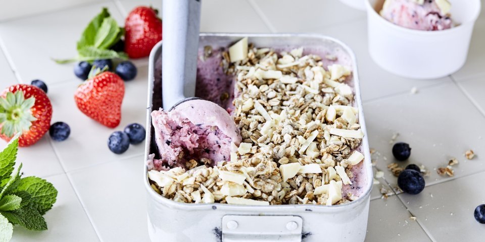 Frozen yoghurt met blauwe bessen en aardbeien Heerlijk yoghurtijs met blauwe bessen en aardbeien. Het ijs komt net uit de vriezer en zit in een box van inox, er is al een bolletje gerold met de ijsschep en ligt te wachten op een kandidaat. We voegden nog vers fruit en een topping van havermout en zonnebloempitten toe voor extra crunch.