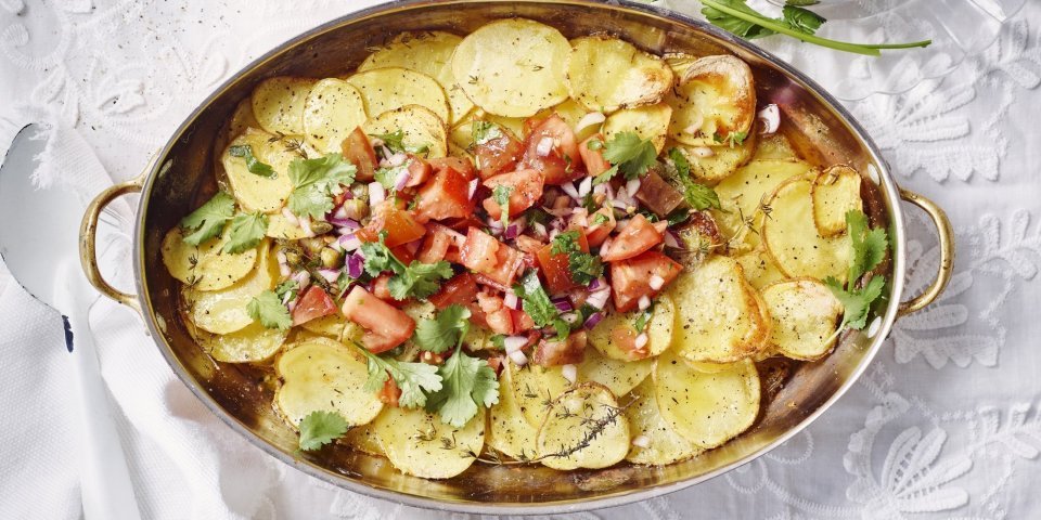 Gegrilde aardappelen met tomatensalsa Aardappelschijfjes liggen gestapeld in een kopere ovenschaal. Hierop is de rode tomatensalsa geschept dat een mooi beeld geven tov het goudgele van de gegrilde patatjes. Her gerechtje is afgewerkt met korianderblaadjes.