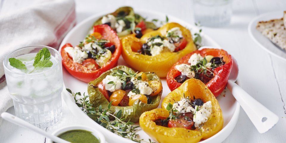 Gegrilde paprika’s gevuld met tomaat en Belgische ricotta Zes halve paprika's liggen op een grote witte schaal. De paprika's zijn opgevuld met kerstomaatjes, olijven en ricottakaas.