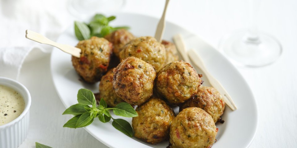 Gehaktballetjes van kip met kaas uit de airfryer Op een wit bordje liggen meerdere gehaktballetjes, sommigen met een prikkertje zodat je meteen van deze knapperds kunt proeven.