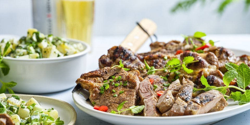 Gemarineerde spiering met aardappelsalade en komkommer Een spieringkotelet ligt op een grote witte schaal in reepjes gesneden. Ze is mooi gegrild en afgewerkt met verse kruiden zoals munt, bieslook en chilipeper die voor extra kleur zorgen. Er is een aardappelsalade bij geserveerd alsook een frisse pint.
