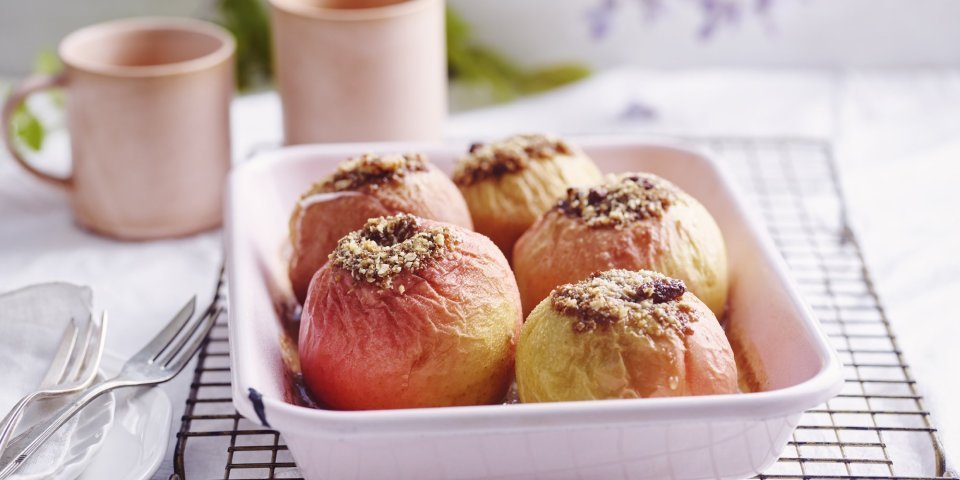Gevulde appel met speculaas, rozijnen en walnoten Gevulde appels in een licht roze ovenschaal. Achteraan staan twee roze kopjes, klaar om aan het ontbijt te beginnen.