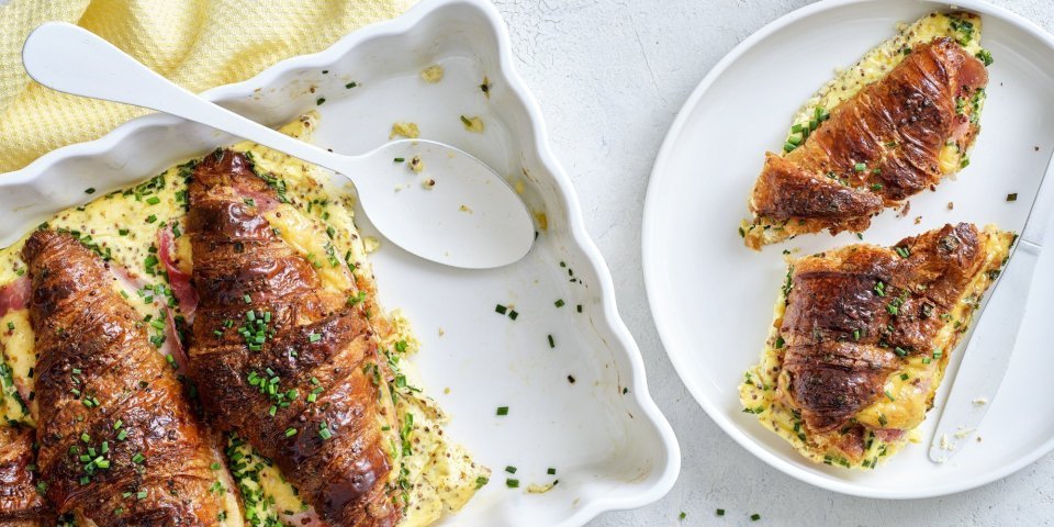 Er staat een witte ovenschotel op tafel gevuld met croissants. Ze zijn doormidden gesneden, bestrijkt met mosterd en belegd met ham en kaas. Daarna is een beslag toegevoegd en werden ze 10 minuten in de oven geplaatst. Om vingers en duimen van af te likken, al zeg ik het zelf.