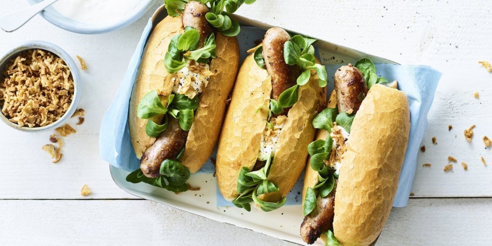 Hotdog met varkensworst 3 hotdogs liggen klaar om gegeten te worden. Ze zijn vergezeld met groene groentjes en een sausje.