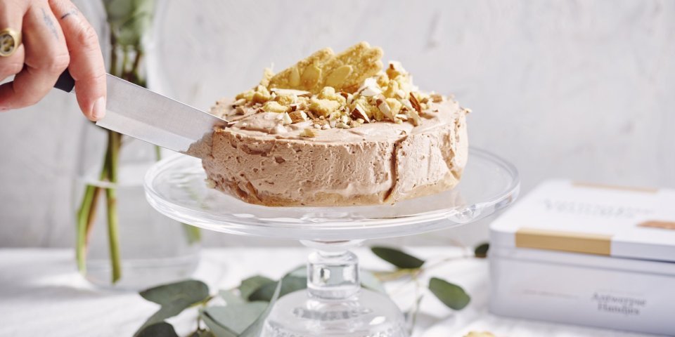 Kaastaart met chocolade en Antwerpse handjes Een heerlijke no-bake taart die niemand koud laat. De cheesecake staat op een hoge taartenschaal en wordt aangesneden. De kaastaart is er eentje met chocolade, Antwerpse handjes en Maltesers. Heerlijk lekker met andere woorden.