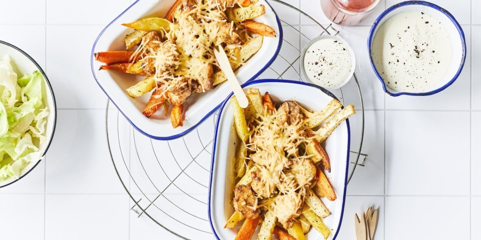 Kapsalon met konijn en groentefrietjes Twee pitaschotels staan op het aanrecht met de ijsbergsla, het yoghurtsausje en de chilisaus langs. Er liggen houten vorkjes langs om meteen van start te gaan aan dit gezond kapsalon.