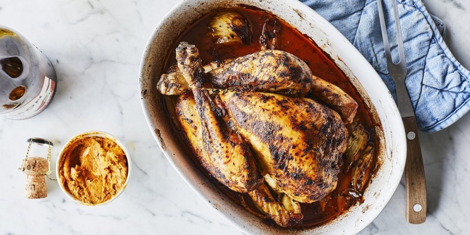 Kip in de oven met cider en beurre café de paris Een heerlijk gegrilde kip uit de oven ligt in een ovenshaal. Ze is heerlijk krokant gebakken en lekker sappig door de homemade kruidenboter. Ze staat op het marmere aanrecht met blauwe nap er langs.