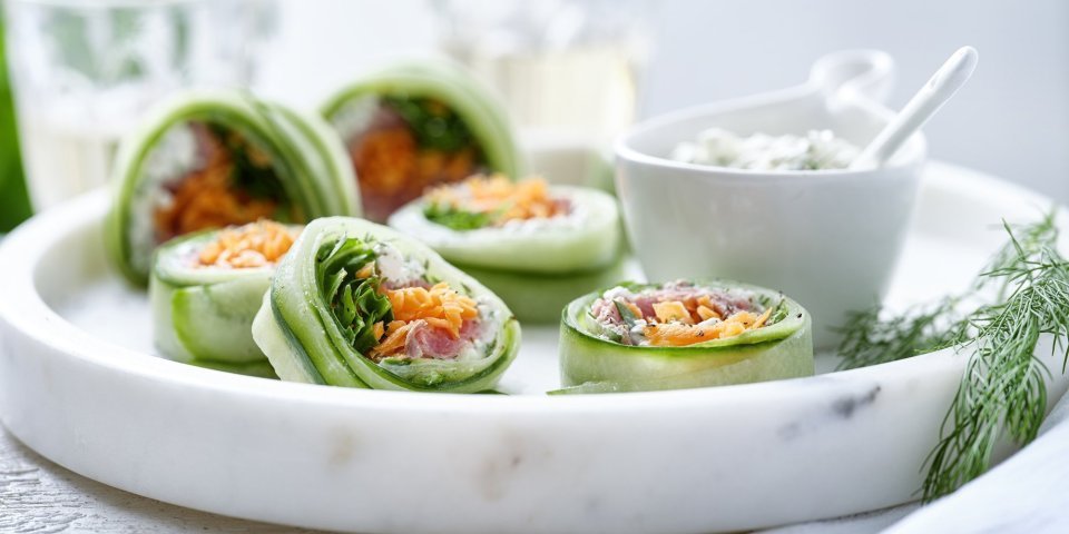 Komkommerrolletjes met cottage cheese en rosbief Rolletjes van komkommer gevuld met cottage cheese, wortel, rucola en rosbief. Een heerlijke gezonde en kleurrijke snack op een bordje van marmer. De overige mengeling met de cheese is geserveerd in een dippotje om eventueel een extra toefje te nemen.