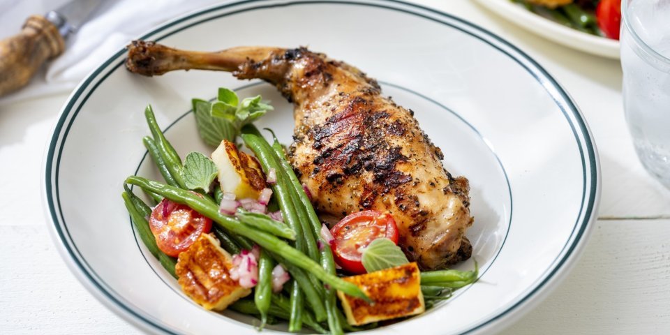 Konijnenbout op de BBQ met een salade van boontjes, tomaat en berloumi In het bord ligt een klaargemaakte bout, ze is heerlijk gegrild van op de BBQ. In het bordje zie je ook een groene bonensalade met tomaat en berloumikaas.