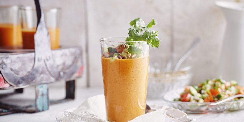 Een gazpacho van paprika geserveerd in een groot glas zorgt intens voor een feestlook. Deze koude soep werd gepimpt met stukjes komkommer en tomaat, als afwerking nog enkele blaadjes koriander en zonnebloempitten bovenop. 