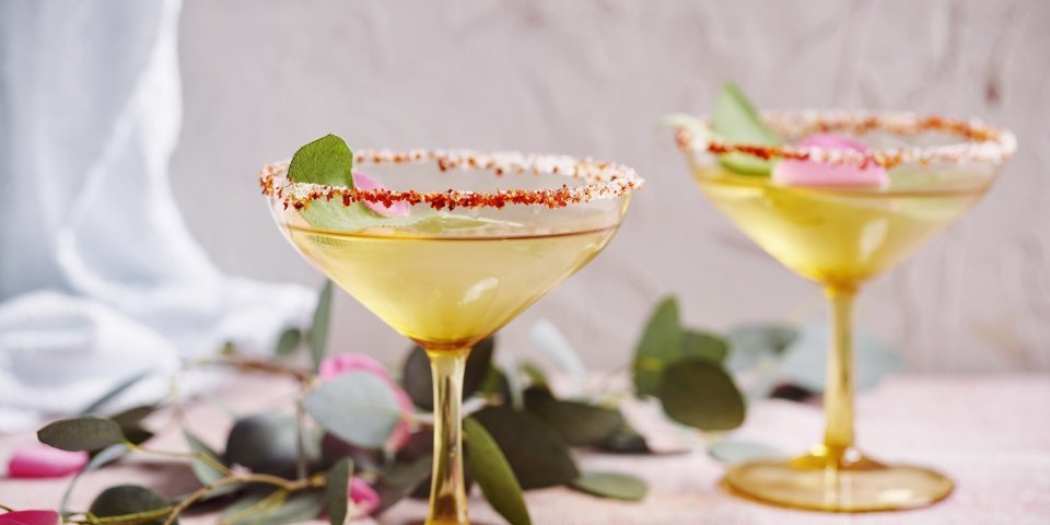 Mocktail van appelsap, vlierbloesemsiroop en salie Twee glaasjes staan klaar om te klinken. De mocktail is geschonken on the rocks en het glaasje is afgewerkt met een kruidig suikerrandje. Ideaal om wat pit in de relatie te brengen.