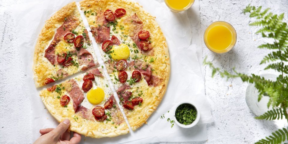 Ontbijt plaattaart met ei, kaas, ham en kerstomaat Een taartje als ontbijt? Yes, we can! Dit is er eentje van bladerdeeg met ei, kaas, ham en kerstomaat. HIj ligt aangesneden in 4 op tafel samen met 2 glaasjes versgeperst fruitsap. Een hand neemt gaat meteen ten aanval om dit heerlijk ontbijt niet koud te laten worden.
