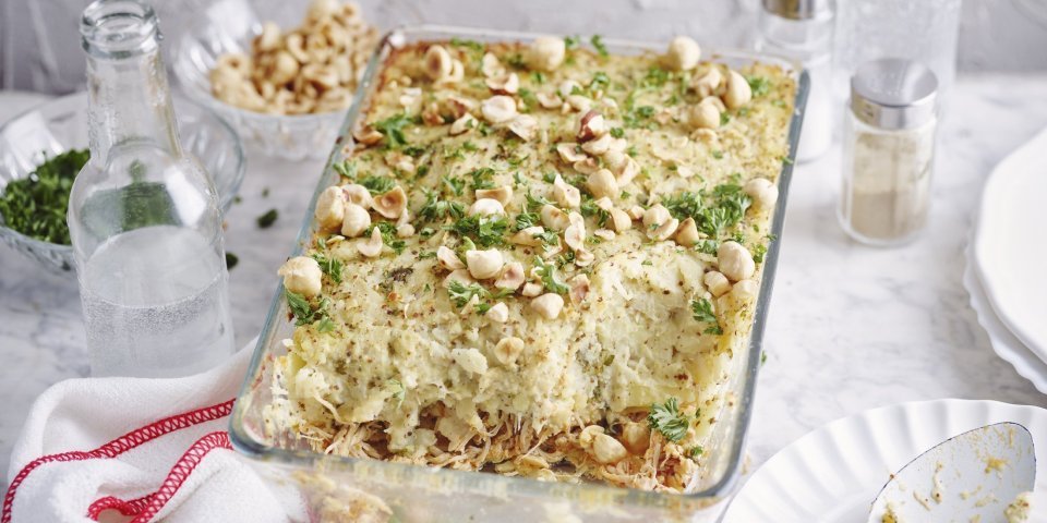 Ovenschotel met pulled chicken en knolselderpuree De ovenschotel met pulled chicken en knolselderpuree staat op tafel, hij is afgewerkt met hazelnoten en peterselie wat een mooie kleur geeft. Er ligt een lepel langs op een klein bordje om meteen uit te scheppen en met het hele gezin aan tafel te gaan.