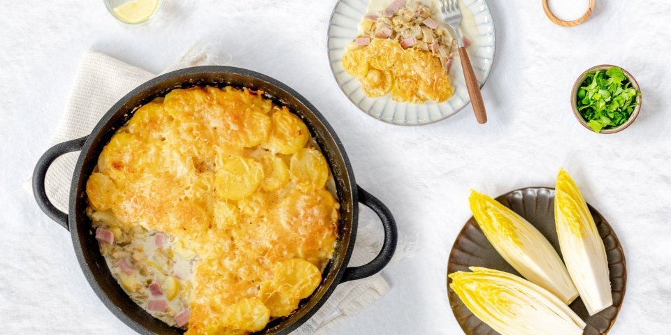 Ovenschotel met witloof, hesp, kaassaus en aardappelen Heerlijke gratin met witloof, hesp, aardappel en veel kaas! De ovenschotel is klaargemaakt in een ronde zwarte ovenschotel, hieruit is al 1 portie uitgeschept.