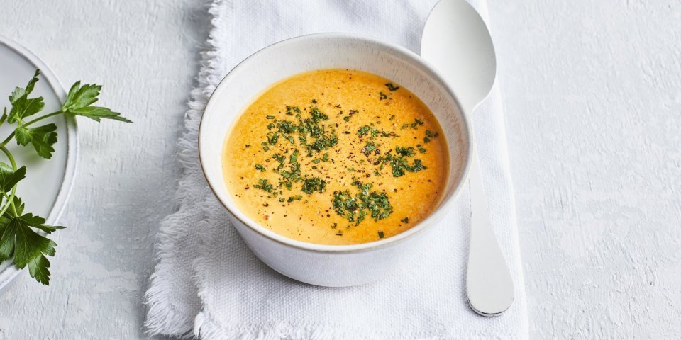 Paprikasaus Deze paprikasaus zit een wit kommetje wat een mooi contrast geeft met de oranje kleur van de saus. Er ligt een witte lepel langs en de saus is afgewerkt met verse groene kruiden.
