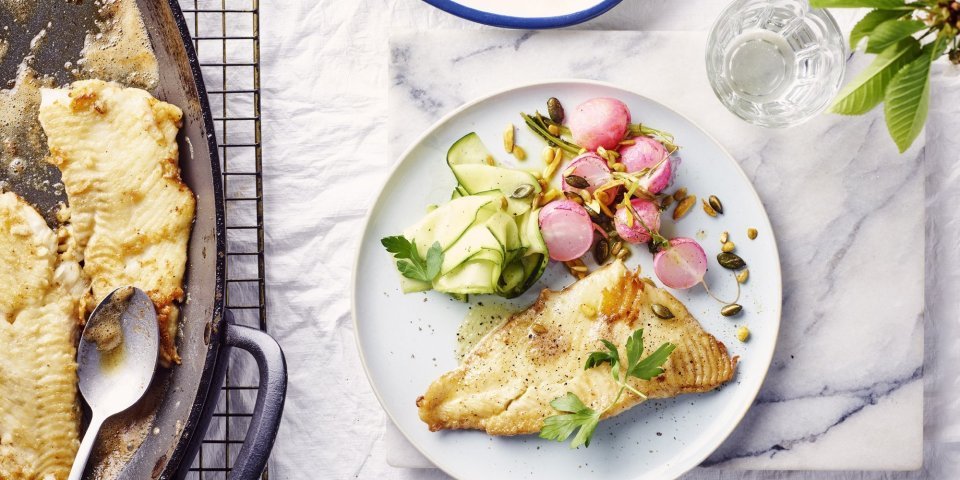 Een rond bord is gevuld met het gerechtje. De grote ovenschaal staat op tafel met al een portie uitgeschept. De radijsjes zitten in een ander ovenschaaltje en staan eveneens op tafel. De radijsjes en courgette zorgen voor een mooie kleur in het gerechtje bij de vis.