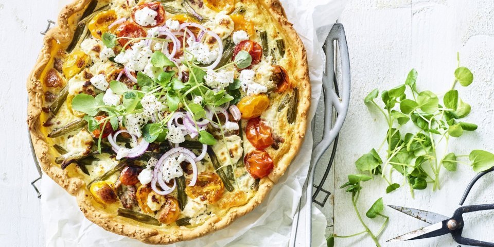 Quiche met boontjes, kerstomaat, lamsgehakt en geitenkaas Kleurrijke quiche gevuld met boontjes, kertomaat, geitenkaas en lamsgehakt. Ja, eentje met gehakt. We werken hem af met verse rode ui en waterkers. Ten aanval!