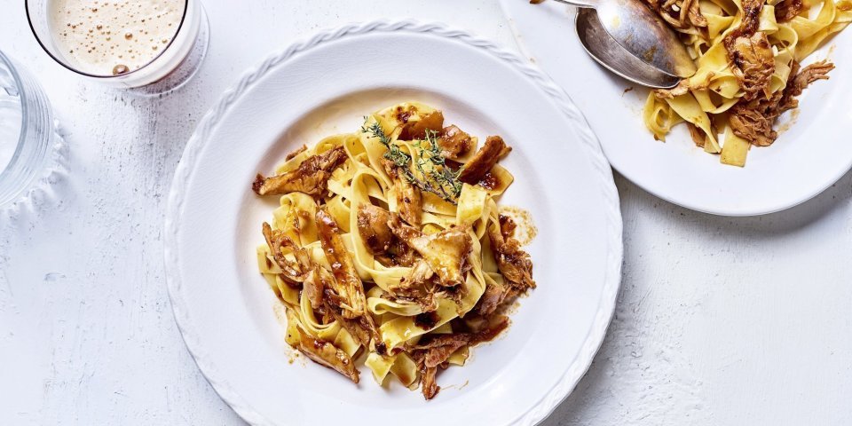 Ragout van konijn met Belgisch bier Op tafel staat een wit bord gevuld met tagliatelle en konijnenragout. Er staat een biertje langs, aangezien de ragout gemaakt is met Belgisch bier.