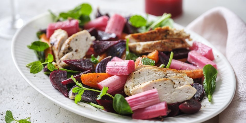 Salade met rabarber, kip en frambozendressing Een rijkgevuld salade die gezond is en mooi van kleur, daar word je instant vrolijk van. De salade bestaat uit frisgroene spinazie, warmoranje wortel, bloedrode bietjes, zoetroze rabarbar en goudgegrilde kip. De frambozendressing werd erbij geserveerd in een glazen kannetje.