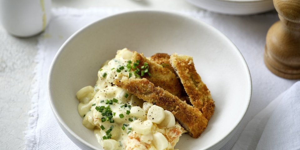 Handgeklopte schnitzel met wortelpuree en schorseneren liggen te blinken in een bordje. De mosterdsaus zit in een sauskannetje en kan je zelf toedienen naar eigen goesting. 