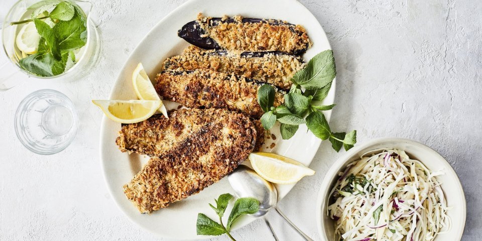 Vegetarische schnitzels gemaakt van aubergine. Ze liggen op een groot wit ovaal bord, waar je er eentje van kan afnemen. Wij serveren hem met een koolslaatje.