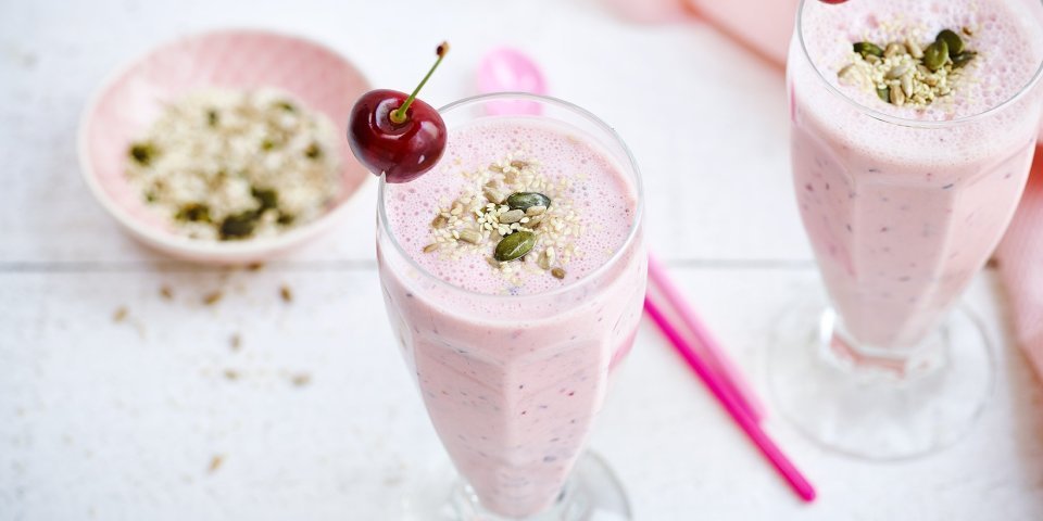 Smoothie van kersen en blauwe bessen Twee rooskleurige smoothies op een witte houten tafel. De smoothie is afgewerkt met een kers en enkele pitjes en zaadjes. Een snel en makkelijk drankje met feestallures!