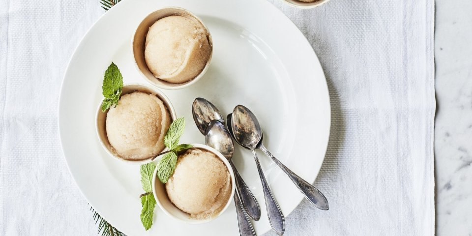 Drie sorbets staan op een wit rond bord, afgewerkt met een muntblaadje. De koffielepeltjes liggen ook op het witte bord, de tafel is aangekleed met takjes kerstboom.